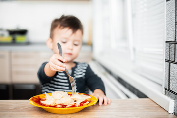 Hungry child eating dumplings in the kitchen, sitting at the table in a gray jacket