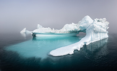 Panorama of a massive iceberg with a smooth underwater shelf on a foggy day. Disko bay, Greenland.