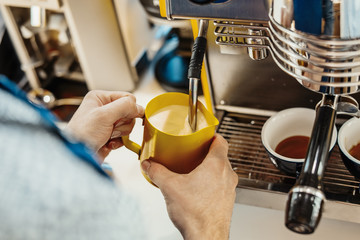 Close up of barista steaming milk in the pitcher with coffee machine.