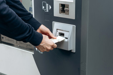Tourist buys tickets for land or underground transport in Germany. Independent purchase of tickets for the tram, bus and train in a modern street machine. Puts money in a special hole in the machine