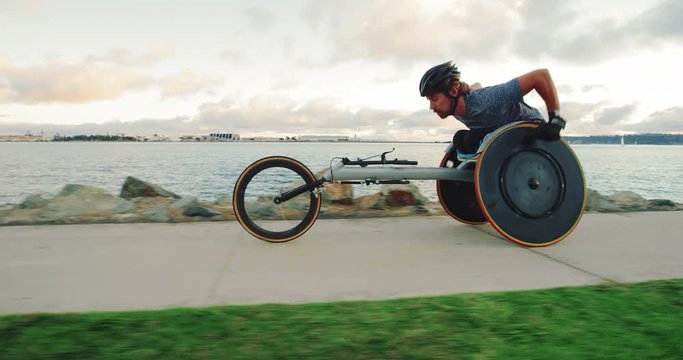 Disabled wheelchair athlete pushing racing chair outside at sunset working out 