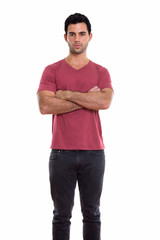 Studio shot of young handsome Hispanic man standing with arms cr