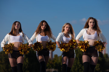 four cheerleader girls with pompoms dance outdoors