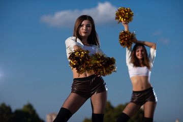 Two girls cheerleaders with pompons dancing outdoors
