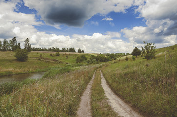 Fototapeta na wymiar Summer landscape with country road.Green hills with trees along the way.Dramatic clouds in the sky.
