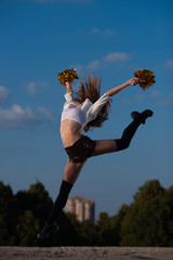 cheerleader girl with pompoms performs acrobatic elements outdoors on sky background