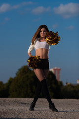 cheerleader girl with pompoms dancing outdoors on sky background