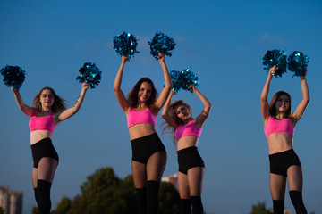four cheerleader girls with pompoms dance outdoors