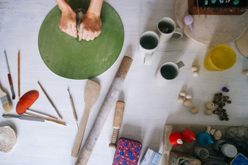 Female hands of a potter crumple clay on a green table, top view