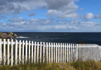 white picket fence with blue ocean and blue cloudy sky 