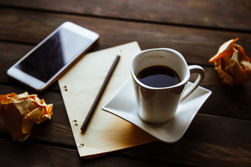 A clean sheet of paper, coffee, phone and a pencil lay on a wooden background, and crumpled sheets lie next