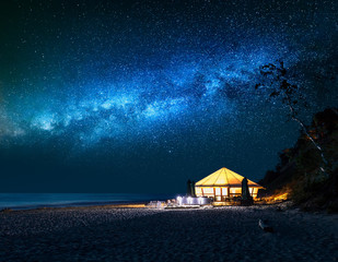 Beach with glowing tent at night with falling stars