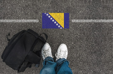  man with a shoes and backpack is standing on asphalt next to Bosnia and Herzegovina flag and border