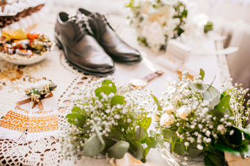 Accessories of a groom: shoes, boutonniere, tie and clock on a wooden surface