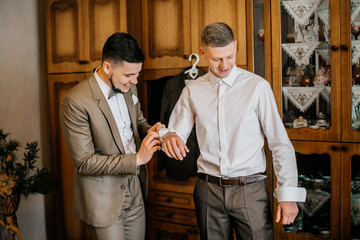 stylish groomsmen helping happy groom getting ready in the morning for wedding ceremony. luxury man...