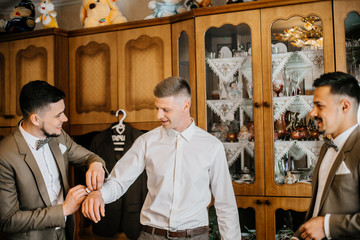 stylish groomsmen helping happy groom getting ready in the morning for wedding ceremony. luxury man...