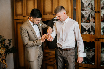 stylish groomsmen helping happy groom getting ready in the morning for wedding ceremony. luxury man...