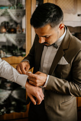 stylish groomsmen helping happy groom getting ready in the morning for wedding ceremony. luxury man in suit in room. Groom preparation before wedding ceremony.