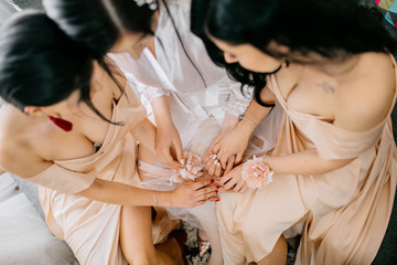 Bridesmaids helping slender bride lacing her wedding white dress, buttoning on delicate lace...