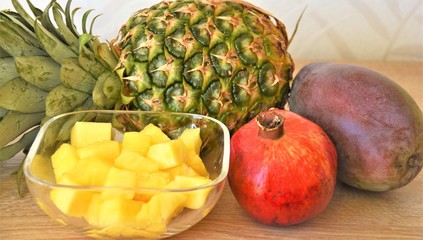 pineapple whole and diced, pomegranate and mango on a wooden table