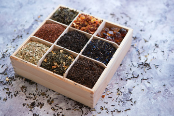 Various kind of dry tea - green, black, red, fruit and blue in wooden box on the table. Top view. Tea time concept.