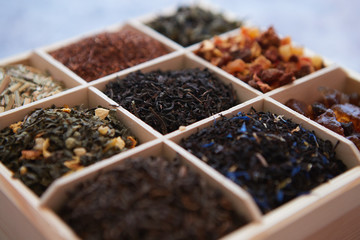 Various kind of dry tea - green, black, red, fruit and blue in wooden box on the table. Top view. Tea time concept.
