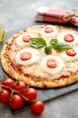 Delicious homemade pizza with tomatoes, mozzarella and basil. Top view with copy space on gray stone table.