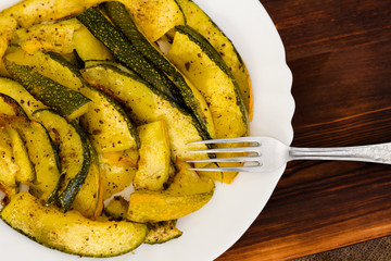 Roasted zucchini in a white plate. Rustic background.