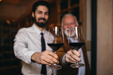 Winemakers in wine cellar holding glass of wine and checking it. Sommeliers testing wines in winery.