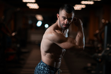 Fototapeta na wymiar Athletic man with a muscular body poses in the gym, showing off his biceps. The concept of a healthy lifestyle