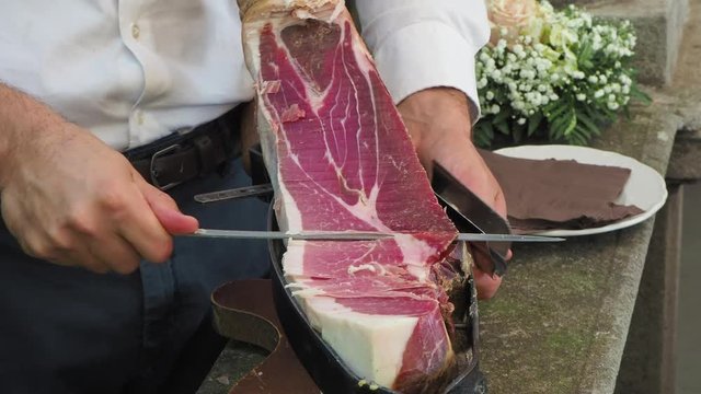 Waiter slices a leg of high quality raw ham