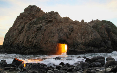 Orange Sunset streams through keyhole arch rock formation in Big Sur