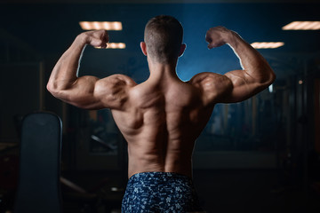 Athletic man with a muscular body poses in the gym, showing off his biceps and back. The concept of a healthy lifestyle