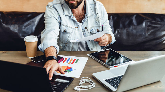 Bearded hipster businessman is working on two laptops in modern office.Man uses computer to enter data. Online marketing
