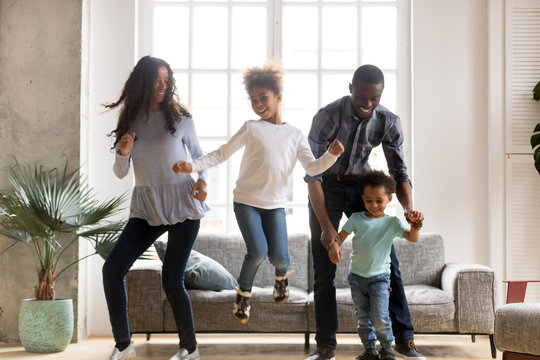 Full length black African whole family have a fun. Married couple with little kids toddler son preschool daughter dancing moving in living room at new home. Happy family spend time together concept