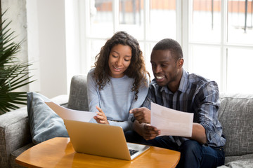 African black positive married couple sitting on sofa at home read documents paper checking bills,...