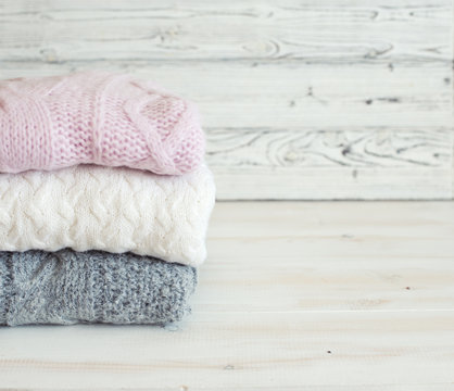 Stack of woolen clothes on wooden white table close up