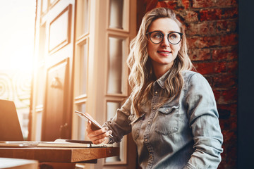 Hipster girl in trendy glasses sits in cafe at table in front of