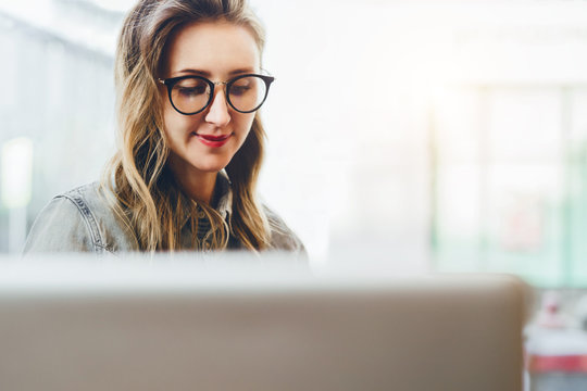 Portrait of young business woman in trendy glasses sitting in cafe,working on laptop.Blogger communicates with followers