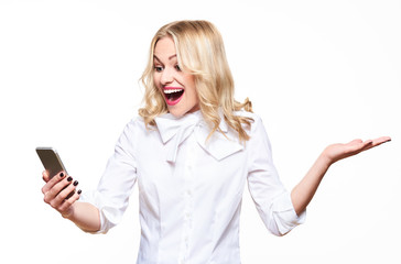 Young gorgeous woman looking at her smartphone over white background, screaming and celebrating victory and success. Very excited, cheering emotion.
