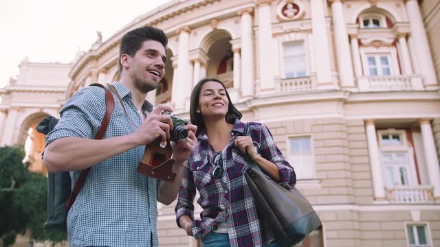 Young mixed race tourist couple taking pictures on vintage camera while walking through the city, slow motion