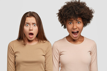Photo of indignant dissatisfied two interracial girls keep mouth widely opened, yell from...