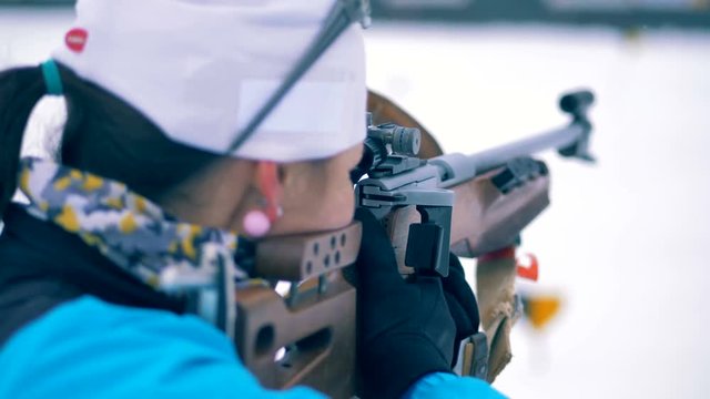 Woman holds a biathlon rifle while aiming at a target. 4K.