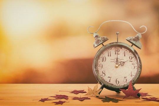 Image of autumn Time Change. Fall back concept. Dry leaves and vintage alarm Clock on rustic wooden table.