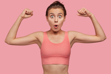 Strength and feminism concept. Surprised young European sportswoman in pink casual top shows hand...