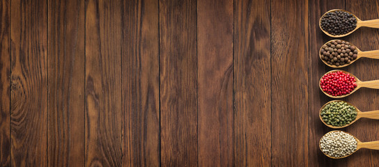 Spices and herbs on wooden table as background for design of packing with food. Collection of spices in spoons with empty space.