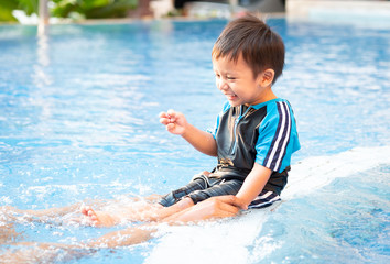 A toddler boy is kicking legs on the edge of a swimming pool