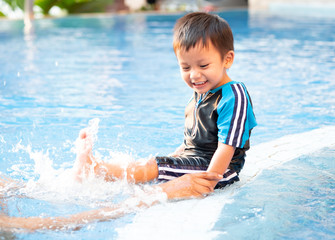 Fototapeta na wymiar A toddler boy is kicking legs on the edge of a swimming pool