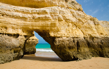 Yellow limestone arch on gold sandy beach Praia da Rocha of the Atlantic Ocean shore with turquoise water near town city of Portimao, Portugal