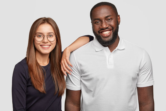 Photo Of Cheerful Lovely Diverse Couple Smile Positively, Stand Next To Each Other, Pose For Making Common Picture, Isolated Over White Background, Enjoy Good Relationships. Positive Emotions Concept